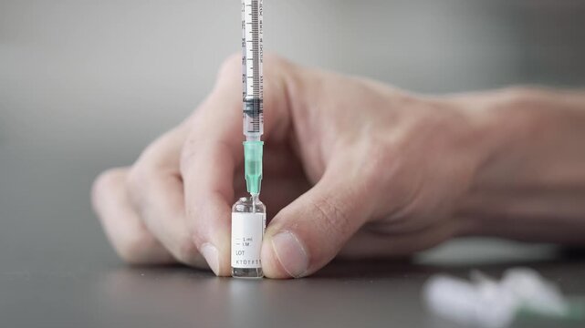 Static close up of fingers holding a small ampoule marked for intramuscular use as a syringe draws the oil in