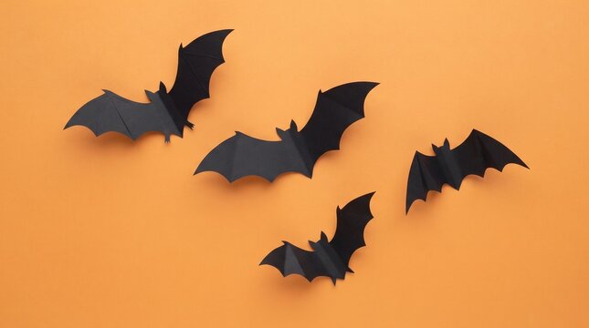 Four black paper bats are arranged on a bright orange background for a halloween themed flat lay composition