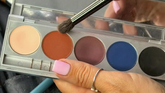 Close up of a makeup brush touching brown eyeshadow in a cosmetic palette, professional beauty tools, makeup preparation and color selection.