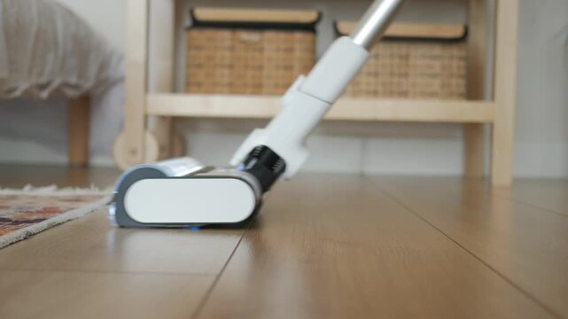 A low-angle dynamic shot of a white cordless vacuum cleaner cleaning wooden floor.
