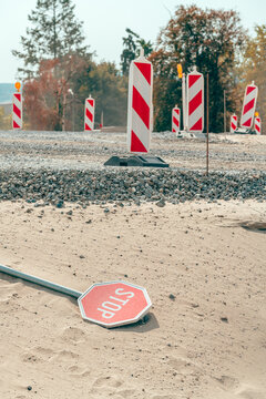 Vertical shot of a red stop sign lying upside down on sandy soil near red and white striped traffic barriers at a roadwork site.