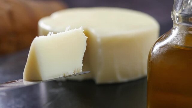 Fresh goat cheese wedge on knife blade close up with honey bottle and round cheese wheel.