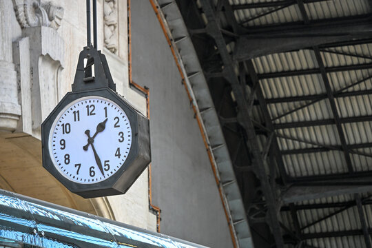 Hanging octagonal clock beneath the roof of a railway station in Milan, Italy
