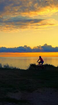 A senior adult enjoys a serene cycling ride along a lakeside path during sunset. The vibrant sky and calm waters enhance the peaceful ambiance, highlighting their active lifestyle and love for nature.