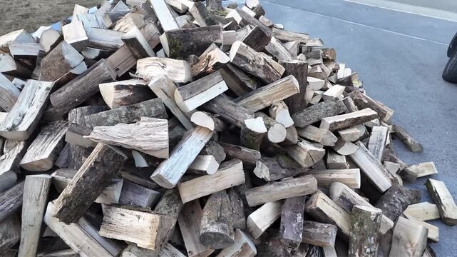 A substantial collection of split timber pieces arranged in a heap on asphalt, ready for use as fuel in a fireplace or wood burning stove heater.