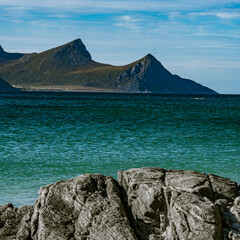 Vertical view of a rocky coastline with turquoise sea water and majestic mountain peaks under a blue cloudy sky in Norway © Quality by Simon