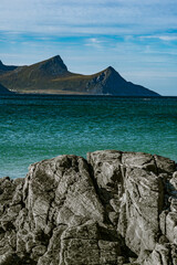 Vertical view of a rocky coastline with turquoise sea water and majestic mountain peaks under a blue cloudy sky in Norway © Quality by Simon