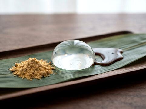 Raindrop cake, clear gelatinous dessert with kinako powder and kuromitsu, on bamboo leaf and wooden tray, traditional Japanese sweet.