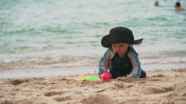 4K Cute baby boy with sun hat playing in the sand on a beautiful beach, close up.