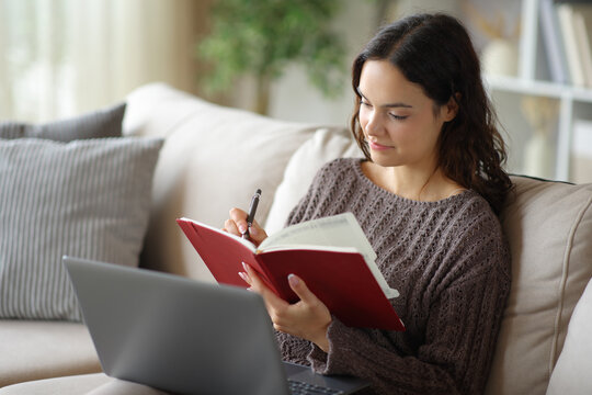 Young woman using laptop and writing in red paper agenda
