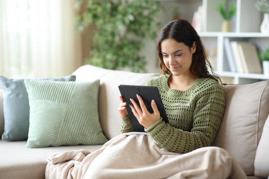 Young woman checking digital tablet covered with blanket in winter