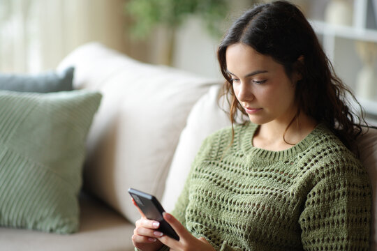 Young woman in green checking phone content on a sofa