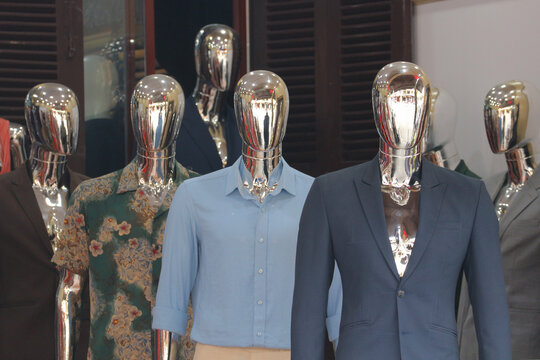 Row of futuristic chrome mannequins displaying tailored men suits and shirts in a clothing shop storefront in Hoi An, Vietnam.