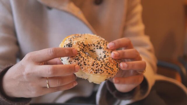 Woman holding fresh toasted everything bagel with sesame seeds and cream cheese in cafe setting.