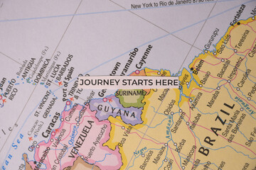 Obraz premium Overhead flat lay of a minimalist paper tag reading journey starts here resting on a physical map of Suriname