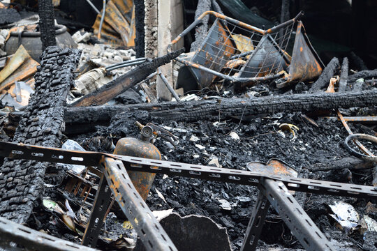 Charred wooden beams rusted metal frames ash scattered debris reveal extensive structural destruction property damage following building fire