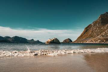 Panoramic view of gentle ocean wave splashing on sandy beach with solitary rock and majestic mountains under blue sky in Norway © Quality by Simon