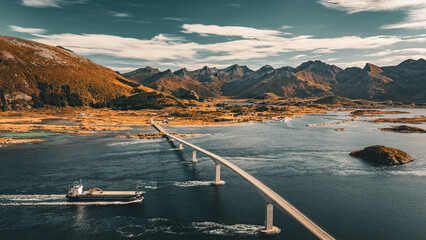 Aerial drone view of a cargo vessel sailing under a long concrete bridge across a sea fjord in scenic Norway landscape with copy space © Quality by Simon