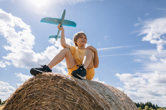 Young boy with toy airplane sits on a hay bale