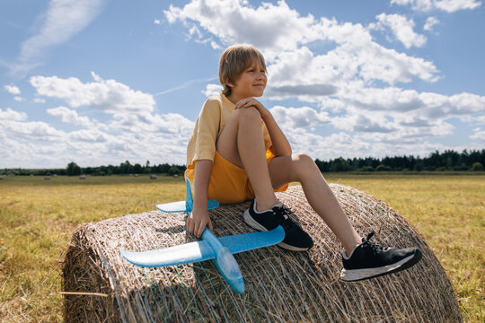 Young boy sitting on a round hay bale with a toy airplane