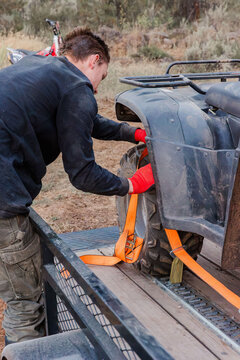 Young man strapping down an ATV onto a trailer for transport