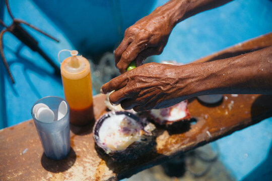 Weathered hands squeezing fresh lime onto oysters on a boat