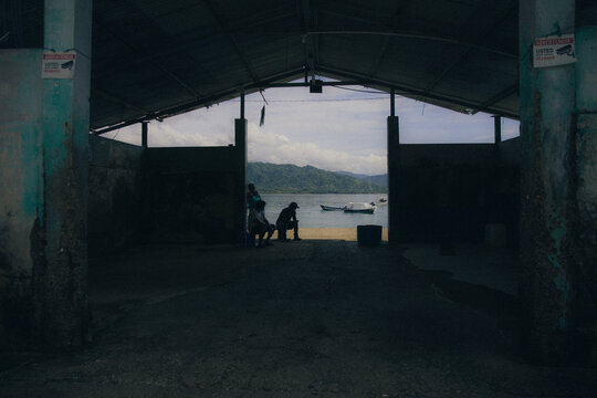 Three people resting in a dark open air boathouse