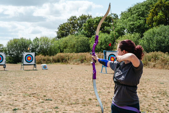 Woman aiming bow and arrow at outdoor targets