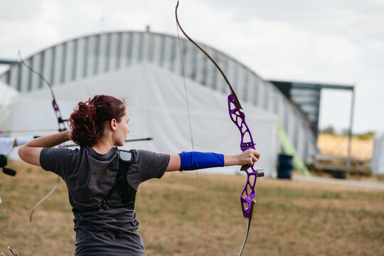 Young woman aiming a purple recurve bow