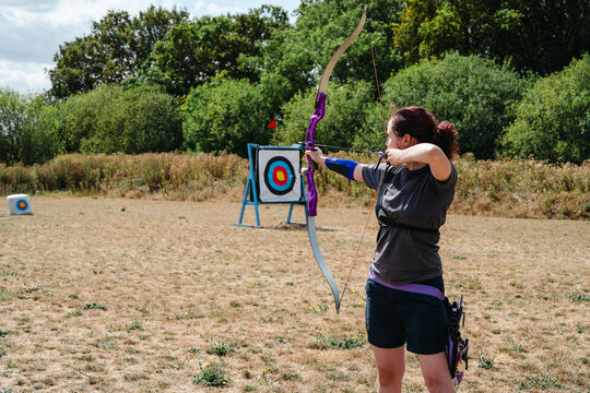 Woman aiming a recurve bow at an outdoor archery target