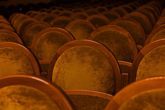 Empty golden brown velvet theater seats in rows inside dark concert hall auditorium background