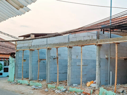 A ground-level view of an ongoing building construction site featuring lightweight concrete block walls supported by wooden props 