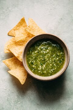 Salsa verde with tortilla chips creates delicious snack. Chips are golden and crispy with textured background. Green salsa adds vibrant color and freshness