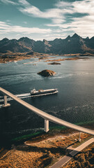 Vertical drone view of a red car driving on a long bridge over a fjord while a cargo ship passes underneath in scenic Norway landscape with copy space © Quality by Simon