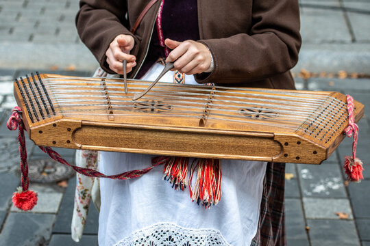 Girl in traditional clothes playing a cimbalom, a type of chordophone composed of a large, trapezoidal wooden box with metal strings