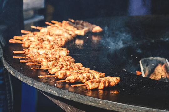 Preparing chicken meat skewers, grilled or roasted on a round griddle or a circular grill in a street food market
