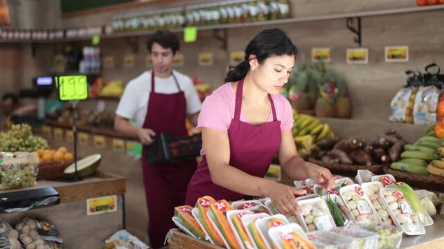 Female salesperson places vegetables and fruits packed in plastic containers on a supermarket display case. . High quality 4k footage