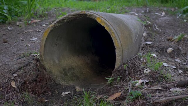 Slow motion close-up of a large cylindrical concrete drainage culvert water sewerage pipe lying submerged in the dirt on a grassy hill terrain outdoors near suburban town Central Coast NSW Australia