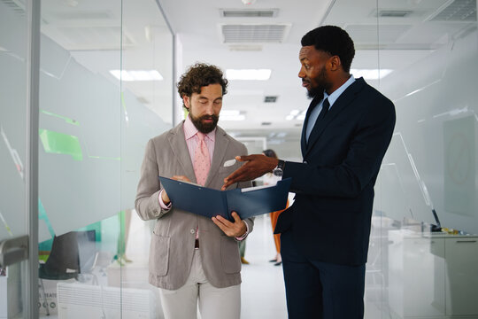 Diverse business professionals discussing documents and collaborating on a project in a modern corporate office corridor, showing teamwork and problem-solving