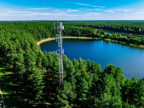 Aerial drone view of a 5G 6G telecommunication tower in a green forest near a scenic blue lake