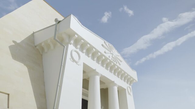 Low angle view shows white pavilion facade with tall columns under blue sky. Classical structure rises upward highlighting clean details