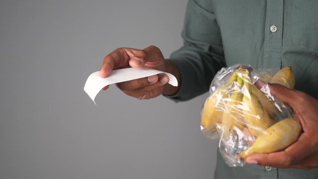 Person holding receipt and bananas in plastic bag at grocery store, shopping concept motion.