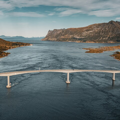 Wide aerial drone view of a long concrete bridge spanning across a sea fjord surrounded by majestic mountains in scenic Norway landscape © Quality by Simon
