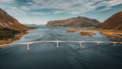 Wide aerial drone view of a long concrete bridge spanning across a sea fjord surrounded by majestic mountains in scenic Norway landscape © Quality by Simon