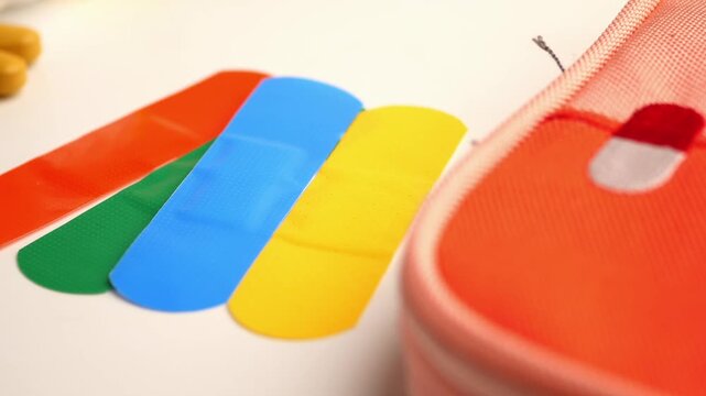 Colorful medical band aids and vitamin pills on white surface with orange first aid pouch.