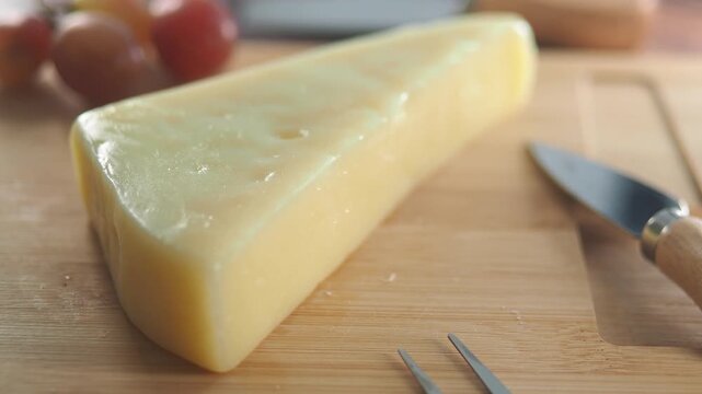 Hard parmesan cheese wedge on wooden cutting board with knife and fork in cinematic motion.