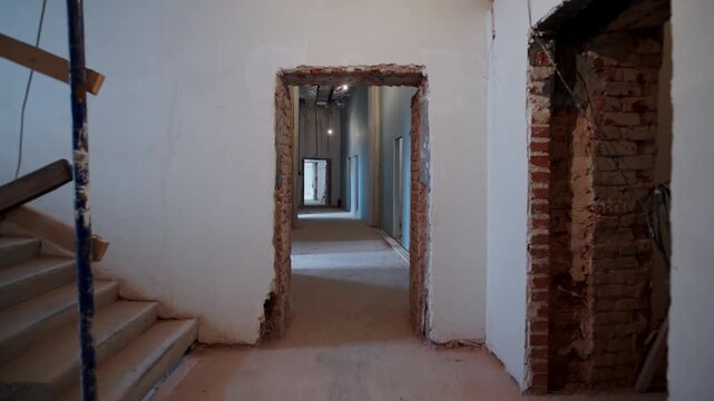 Exposed brick doorways connect unfinished rooms along narrow passage. View centers open entrances revealing raw renovation structure