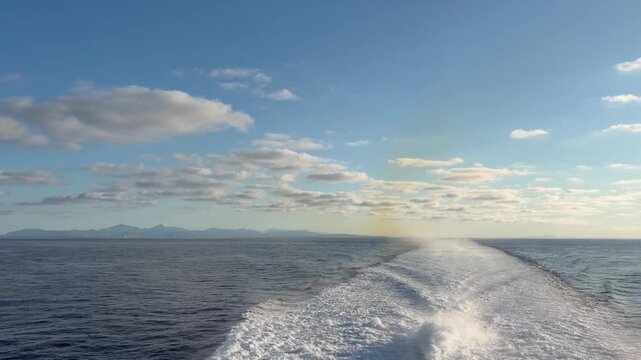 Ocean view from a moving boat with distant mountains and blue sky seascape featuring calm water