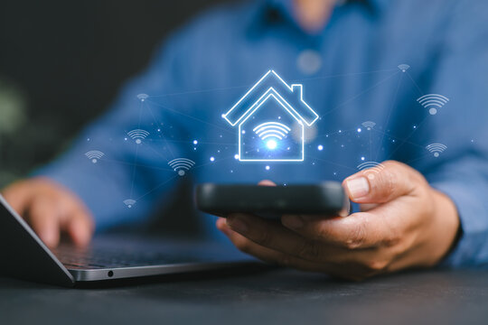 Smart Home Technology with Wireless Network Control. Man using smartphone and laptop with Wi Fi and house icons, symbolizing IoT connectivity, remote access, and modern digital lifestyle at home.