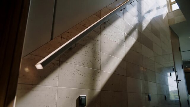 Panning camera revealing metal handrail on stairwell, sunlight shifting to reveal skylight corridor